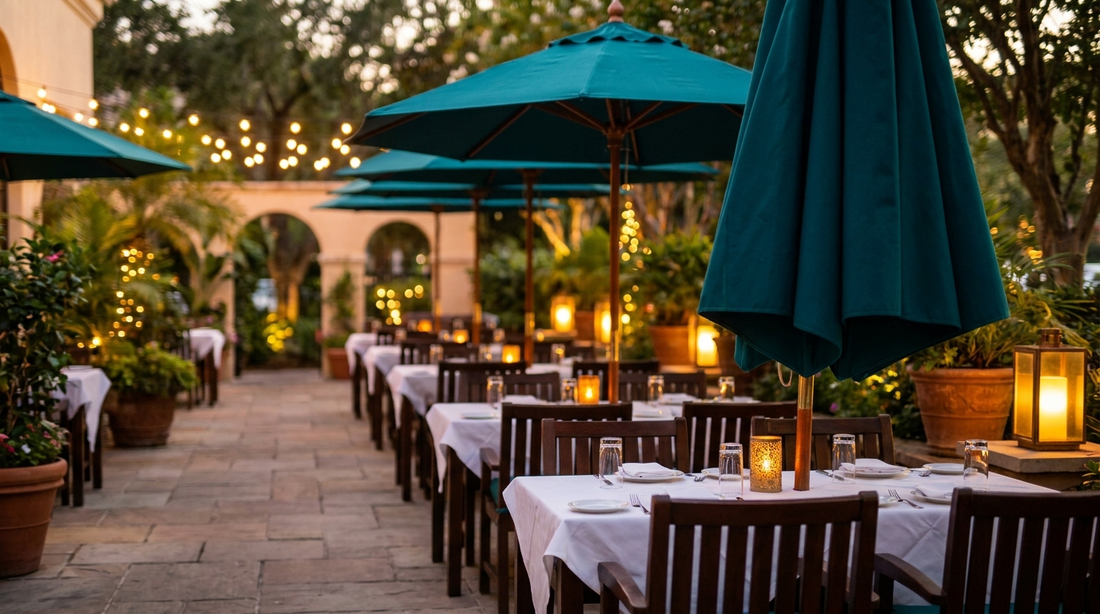 An upscale restaurant patio with a row of matching teal branded garden umbrellas over outdoor dining tables in the evening
