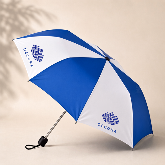 A blue and white folding umbrella with the brand name 'DECORA' printed in blue on alternate panels, shown open against a warm beige background with soft leaf shadows.