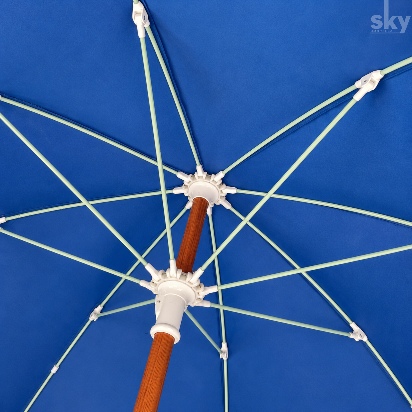 Close-up underside view of a blue patio umbrella showing the wooden look pole finish, white canopy attachments, and light green ribs against a blue fabric surface.