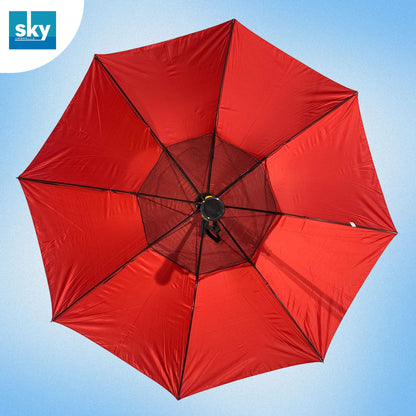 A large red Fan umbrella viewed from directly above, showing its canopy panels, ribs, and central black mesh hub against a light blue sky. 