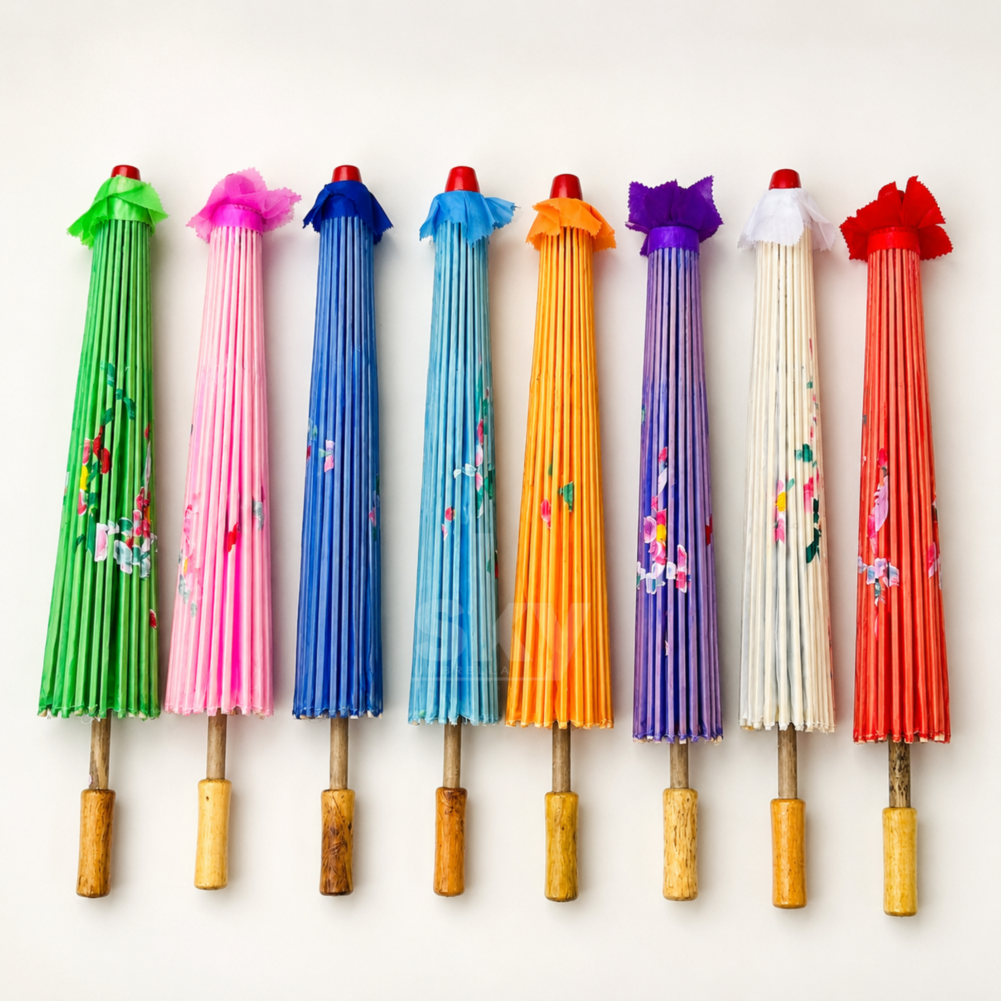 Eight traditional Japanese folding umbrellas in various vibrant colors (green, pink, blue, light blue, yellow, purple, white, red) are lined up horizontally against a clean white background. Each umbrella features pleated fabric, hand-painted floral details, and a decorative fabric ribbon at the top.