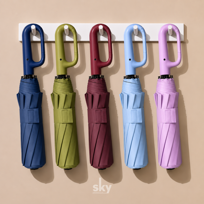 Five compact 3 fold travel umbrellas in dark blue, green, maroon, light blue, and pink are hanging from a white wall-mounted rack against a warm beige background.