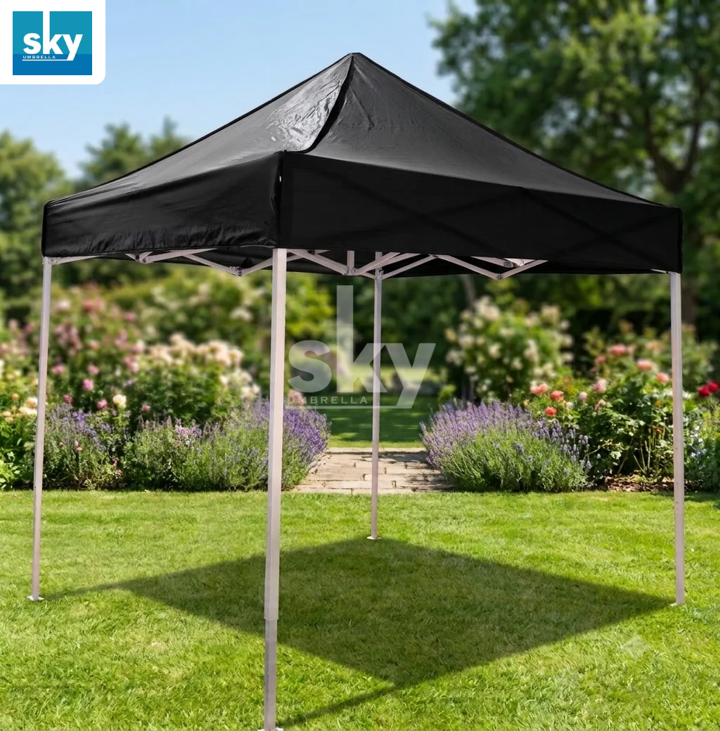 A black pop-up canopy tent with a white metal frame set up on a green lawn in a garden.