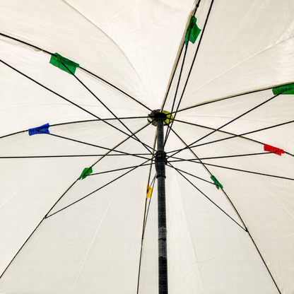 The underside of a white umbrella viewed from below, showing the black metal ribs, central hub, and small colored plastic tips in green, blue, red, yellow, and black.