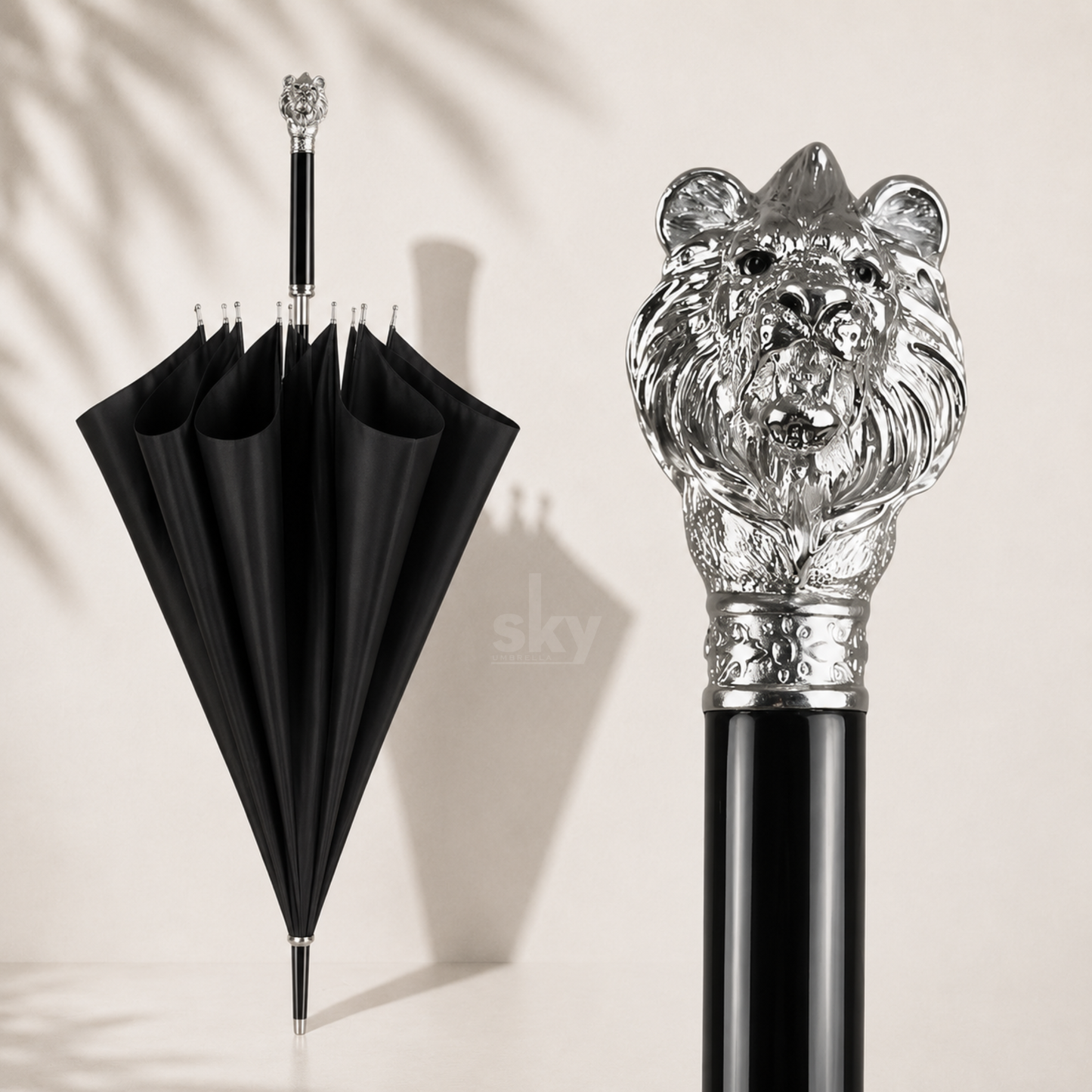 A luxury black umbrella shown partially open on the left and a close-up of its ornate silver lion head handle on the right, set against a warm beige background with soft leaf shadows. Perfect for custom brand printing and gifting.