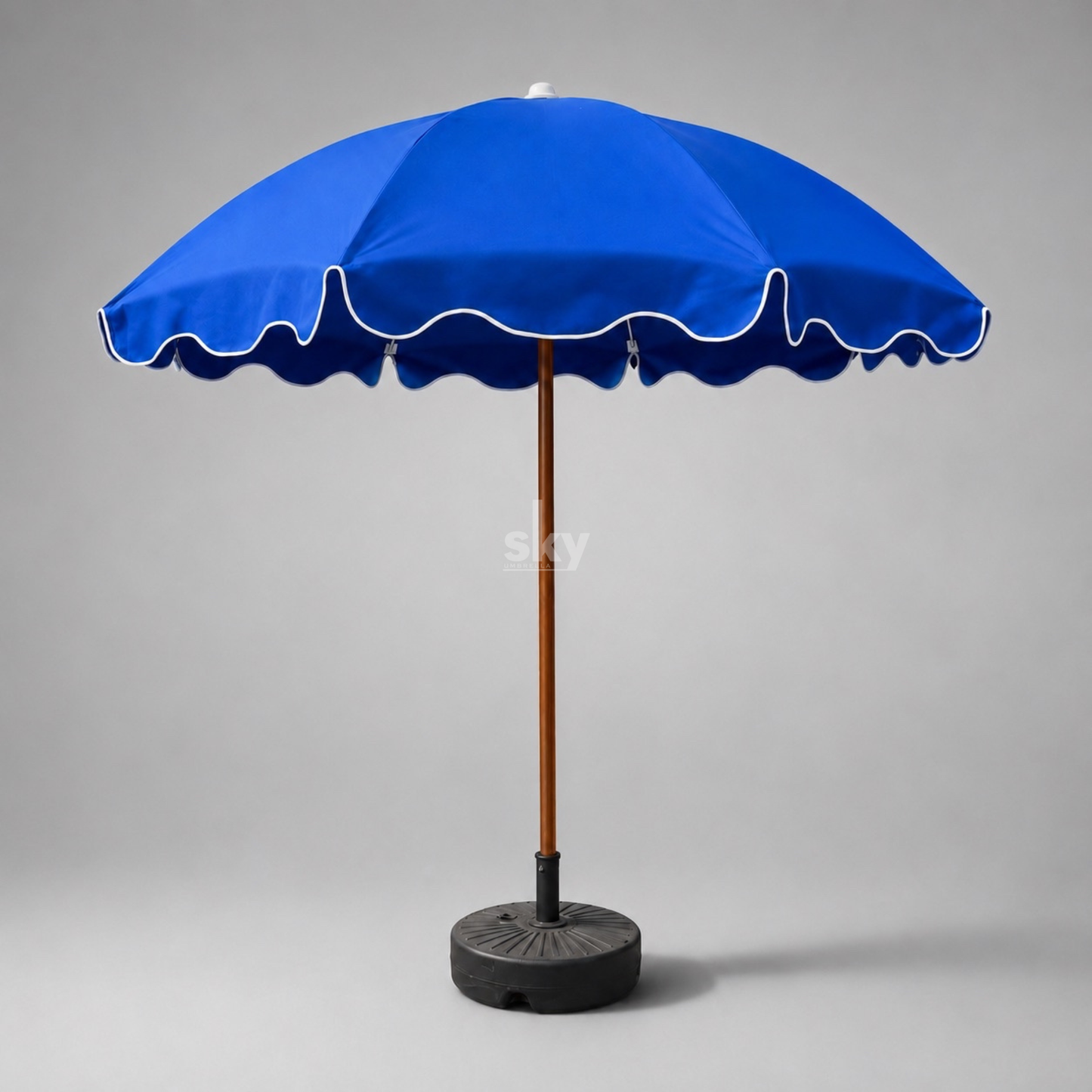 A blue patio umbrella with a scalloped edge, blue piping, a brown pole, and a black weighted base on a white background