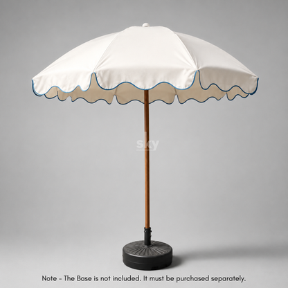A white patio umbrella with a scalloped edge, blue piping, a brown pole, and a black weighted base on a white background.
