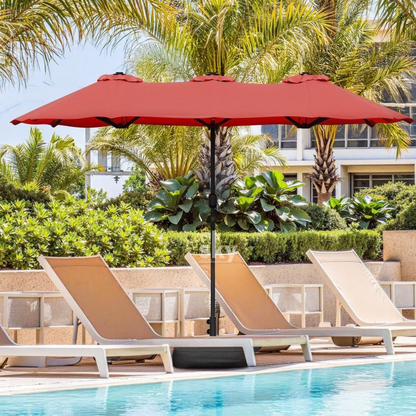 A Maroon patio umbrella with a black central pole stands over three beige lounge chairs beside a swimming pool, with palm trees and resort-style buildings in the background.