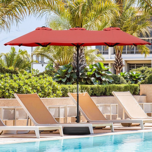 A Maroon patio umbrella with a black central pole stands over three beige lounge chairs beside a swimming pool, with palm trees and resort-style buildings in the background.