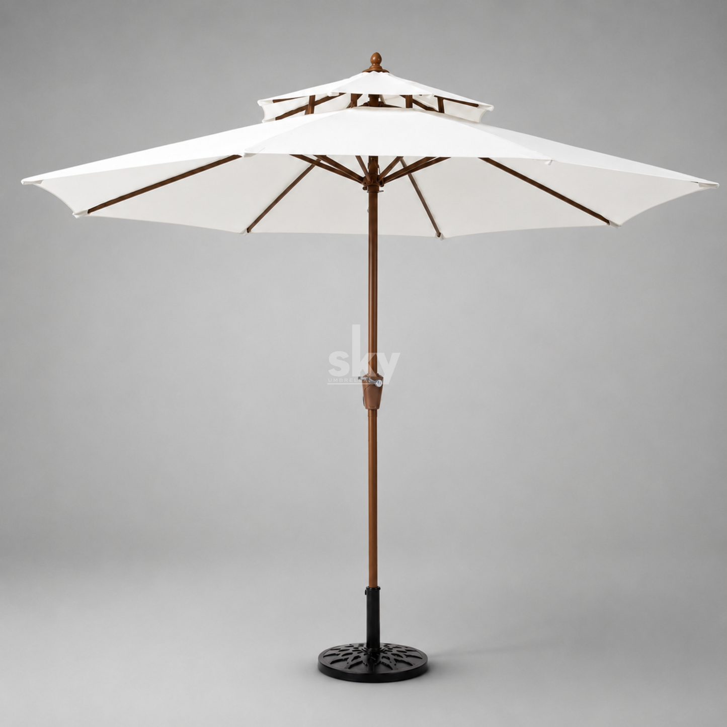 A double-tiered patio umbrella with off-white fabric canopy panels and a brown wooden finish pole, standing on a black metal base against a neutral gray background.