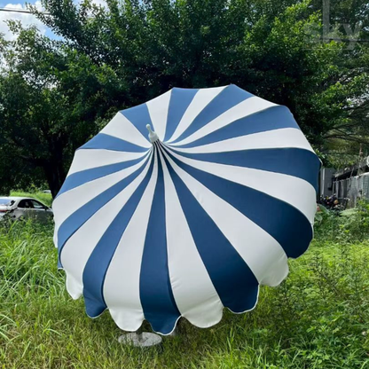 A large patio umbrella with alternating navy blue and white radial stripes, set outdoors on a grassy lawn with trees in the background.
