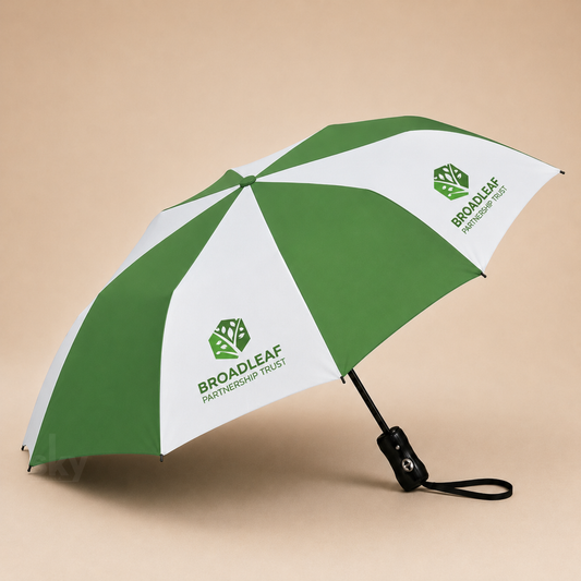 A green and white striped folding umbrella with the Broadleaf Partnership Trust logo printed on the canopy, shown open on a beige background.