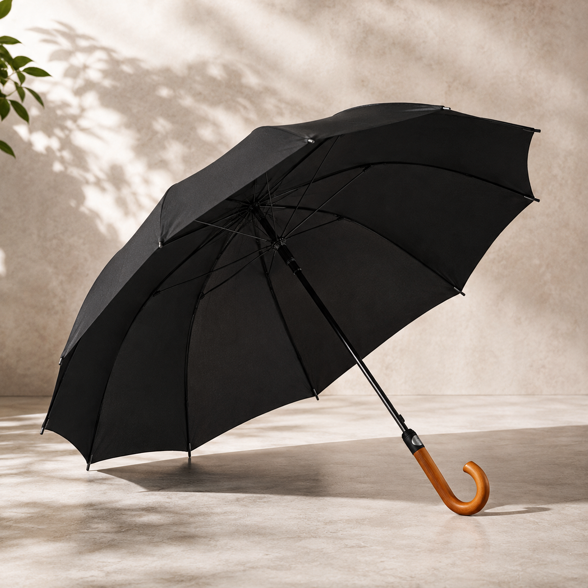 A black open umbrella with a curved light brown wooden handle, photographed on a beige floor against a textured beige wall. With custom brand logo printing available.