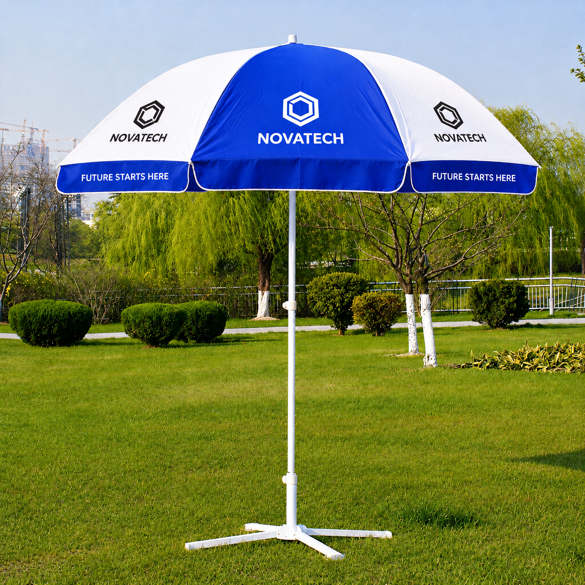 A blue and white  branded outdoor patio umbrella with a white tripod base, set on a green grass lawn with trees in the background.