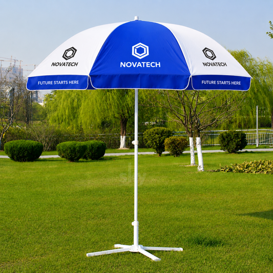 A blue and white  branded outdoor patio umbrella with a white tripod base, set on a green grass lawn with trees in the background.