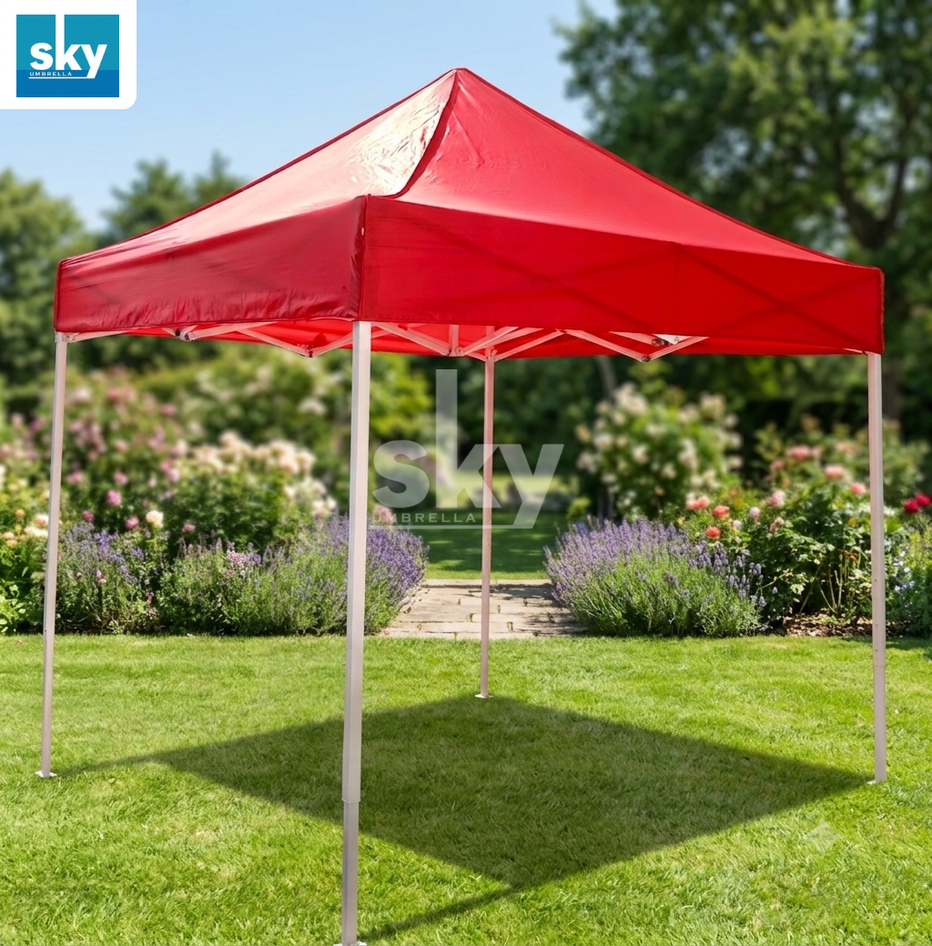 A red pop-up canopy tent with white support legs set up on a green lawn in a garden setting.