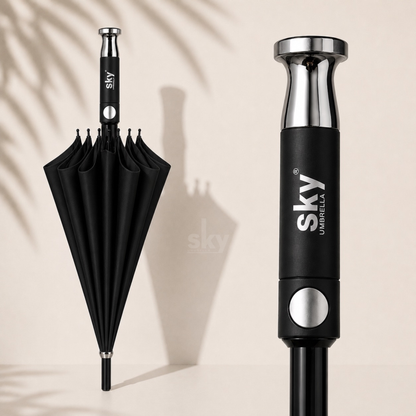 A black umbrella shown closed on the left and a close-up of its handle on the right, both on a light beige background with soft palm shadow overlays. The handle is black with a silver metallic top and button, and the brand name 'sky UMBRELLA' is printed on the handle.